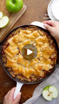 an apple pie in a cast iron skillet on a wooden table with apples around it