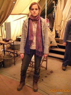 a woman standing in front of a tent wearing boots and a scarf around her neck