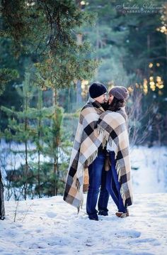 two people standing in the snow with a blanket wrapped around their shoulders and looking into each other's eyes