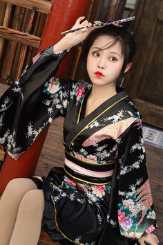 a woman in a black and pink kimono sitting on a wooden floor next to a red pole