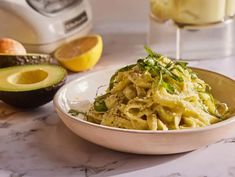 a white bowl filled with pasta next to an avocado