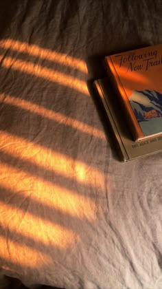 an orange book sitting on top of a bed next to a white sheet with the sun shining through it