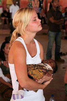 a woman holding a baby in her arms while people watch from the ground behind her