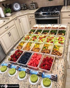 a kitchen counter topped with lots of trays filled with fruit and veggies