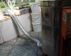 a dirty kitchen with an old washing machine and buckets on the floor next to it