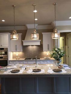 a large kitchen island with lights hanging from it's ceiling and two ovens in the background