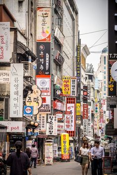 people walking down an alley way with many signs on the buildings and billboards above them