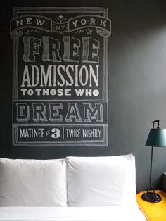 a bedroom with a chalkboard on the wall and a white bed in front of it