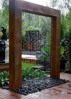 an outdoor fountain in the middle of a wooden deck with rocks and plants around it