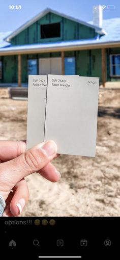 someone is holding up two cards in front of a house