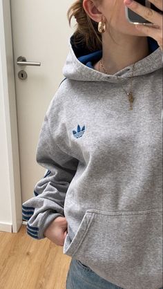 a woman in a grey adidas hoodie talking on her cell phone while standing next to a door