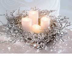 four white candles are lit on a silver tray with branches and leaves around it, surrounded by crystals