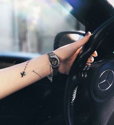 a woman's hand on the steering wheel of a car with a star tattoo