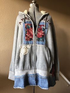 a gray hoodie with flowers on it is hanging from a coat hanger in front of a tan wall