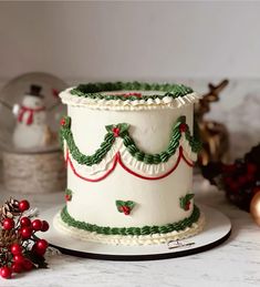 a white cake with green and red decorations on it sitting on top of a table