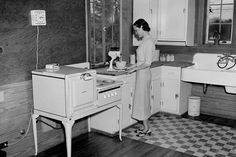 an old photo of a woman washing dishes in the kitchen with her stove and dishwasher