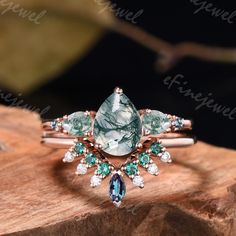 a green and white stone ring sitting on top of a piece of wood with diamonds