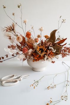 a white vase filled with lots of different types of flowers next to scissors and plants