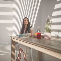 a woman sitting at a wooden table with plates and cups on it, looking up