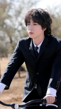 a man in a suit and tie riding a bike on dirt ground with trees in the background