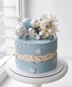 a blue cake with white snowflakes and a teddy bear on top