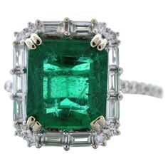 This stunning 3.16 carat weight green emerald fashion ring is a gorgeous and eye-catching choice for any occasion. The emerald is a beautiful shade of green and boasts exceptional clarity and brilliance, weighing in at 3.16 carats. It is set in luxurious 18K white gold and is surrounded by a halo of 32 round diamonds, totaling 0.74 carats, that are set in a pave setting. Gia Certified Dazzling Green Diamond Ring, Gia Certified Green Diamond Ring, Green Emerald Cluster Ring In Platinum, Green Cluster Emerald Ring Vvs Clarity, Cluster Green Emerald Ring In Platinum, Cluster Emerald Ring With Vvs Clarity, Green Cluster Emerald Ring With Vvs Clarity, Green Platinum Emerald Ring With Cluster Shape, Platinum Cluster Emerald Ring