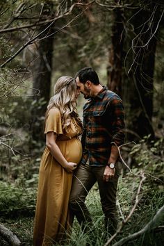 a pregnant couple is standing in the woods with their arms around each other and kissing