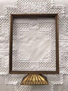 an old photo frame on top of a table with white doily and gold trim