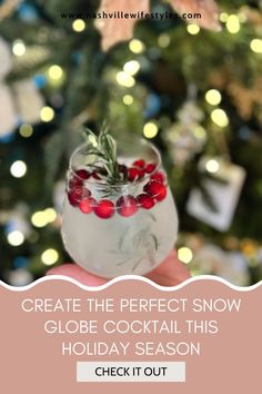 a person holding up a glass filled with cranberries and greenery in front of a christmas tree