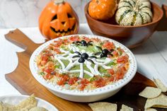 a white bowl filled with guacamole and black olives next to two pumpkins