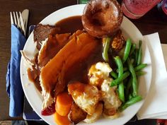 a white plate topped with meat covered in gravy next to green beans and mashed potatoes