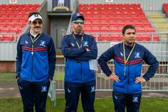 three men standing in front of an empty stadium