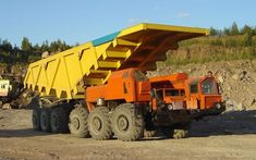 an orange dump truck parked in front of a yellow dumpster on a dirt road