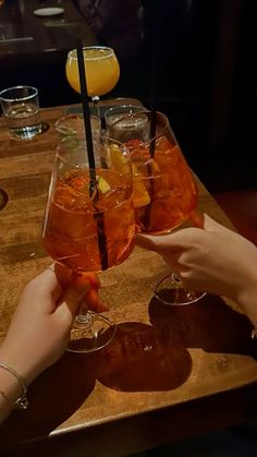 two people are toasting with drinks in glasses on a wooden table at a restaurant