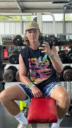 a man sitting on top of a red chair in a gym holding a cell phone