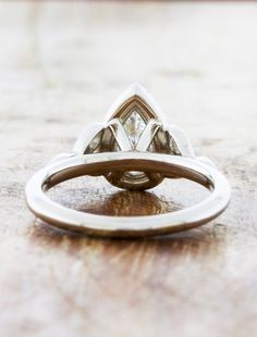 an engagement ring with three pear shaped diamonds on it's side, sitting on top of a wooden table