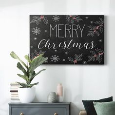 a black and white merry christmas sign on a wall above a gray chest of drawers