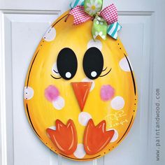 a painted yellow bird with polka dots on it's face is hanging from a white door