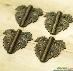 four antique brass leaves with holes in the middle on a wooden surface, set against a white background