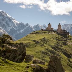 an old castle sitting on top of a green hill with mountains in the back ground