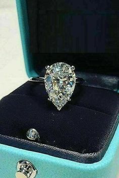 an engagement ring with a pear shaped diamond sits in a blue box on a white surface