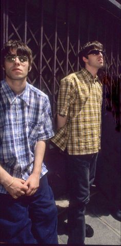 two men standing next to each other in front of a metal structure and wearing sunglasses