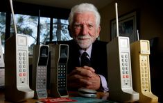 an older man sitting at a table with four old cell phones on top of it