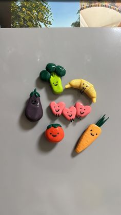 small plastic fruits and vegetables are arranged on a table top, with faces drawn on them