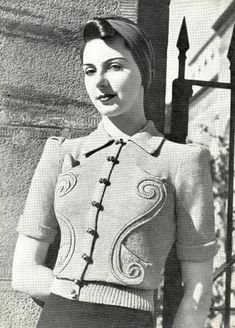 a woman standing in front of a building wearing a sweater and skirt with buttons on it