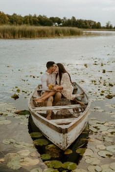 a man and woman sitting in a small boat on the water surrounded by lily pads