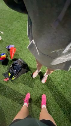 two people standing in the grass with their feet propped up next to bags and backpacks