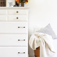 a white dresser sitting next to a window filled with flowers