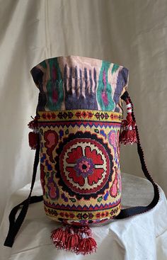 "Medium Drawstring Silk Petit Point Handbag created and handmade in Uzbekistan. Trimmed and Lined with silk and cotton ikat fabric, hand woven silk strap with tassels and a drawstring closure. Each handbag is hand drawn onto cotton canvas, inspired by original designs from Uzbekistan textile history.  8\" high x 8.5\" width(17\" in diameter), top opening 17\" wide, approx. 57\" strap x 3/4\" width. Drawstring goes through ikat channel and has tassels at the opening of the channel. Fits largest s Traditional Multicolor Bucket Bag, Traditional Multicolor Bucket Bag For Daily Use, Traditional Woven Shoulder Bag, Traditional Handmade Multicolor Bucket Bag, Traditional Multicolor Handmade Bucket Bag, Bohemian Embroidered Tapestry Bags, Traditional Embroidered Tapestry Bags, Traditional Woven Bucket Shoulder Bag, Traditional Woven Pouch Bag