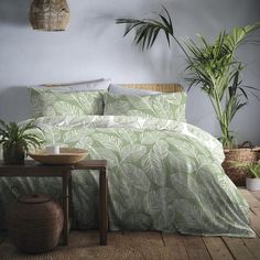 a bed with green leaves on it in a room next to a table and potted plants